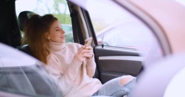 Online dating concept - a 30-year-old woman communicates with her boyfriend online messages via smartphone while sitting in a car in a parking lot. 4k footage