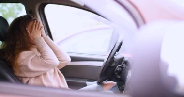 4k footage of a 30-year-old woman receives a message while sitting in a car in a parking lot and becomes insanely upset. She drops the phone and grabs her head.