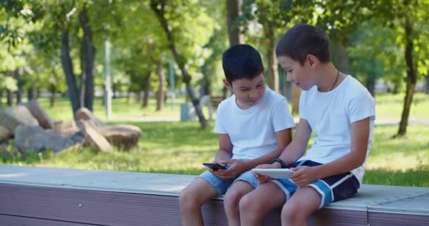 Footage Two Boys Playing Smartphones While Walking Outdoors Sitting Bench — ストック動画