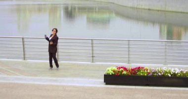 Bir iş kadınının gezinti güvertesinde dans edişine yakınlaşın. Çevrimiçi akıllı telefon uygulaması kullanarak kulaklıkla müzik dinliyor. Yavaş çekim 4k görüntü.