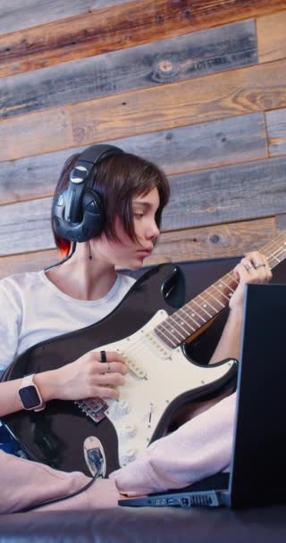 在网上吉他课上 一个少女的4K的垂直镜头 她坐在家里 在笔记本电脑监视器前的耳机里拿着吉他 慢动作视频 — 图库视频影像