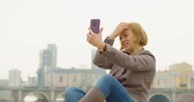 Online dating concept. 40 year old woman sits on the street with a phone and chats animatedly with her boyfriend through an online video call. 4k footage.