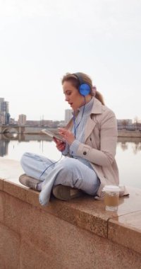 Ofis telaşından ve şehir gürültüsünden uzak dur. Kulaklıklı genç bir kadın sette rahatlatıcı müzik dinliyor. Dikey 4k görüntü.