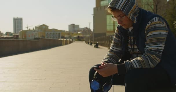 Подросток Смартфоном Наушниками Болтает Друзьями Свежем Воздухе Зависимость Смартфонов Кадров — стоковое видео