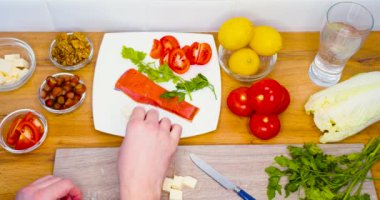 Top view - male hands put sliced cheese on a plate with fish and herbs. Cooking. Keto diet and healthy low carb diet for weight control. Vertical slow motion 4k footage.