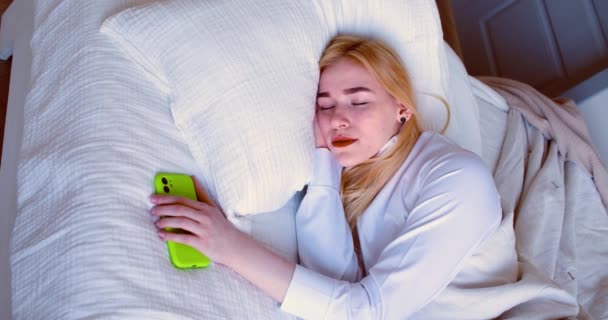若い女性が目を覚ます 彼女のスマートフォンでメッセージをチェックし 眠りに落ちる ソーシャルメディア中毒の概念 スローモーション4K映像 — ストック動画