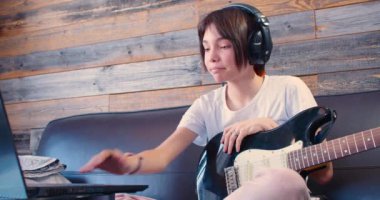 Teenager girl with guitar in headphones in front of laptop monitor. She listening to the sound of her recorded guitar. Slow motion 4k footage.