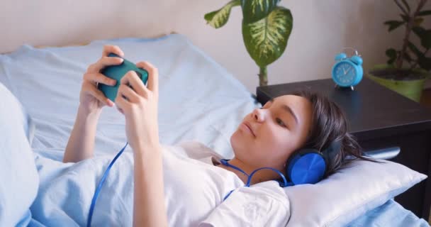 Девушка Постели Смартфоном Слушает Музыку Играет Игры После Пробуждения Концепция — стоковое видео