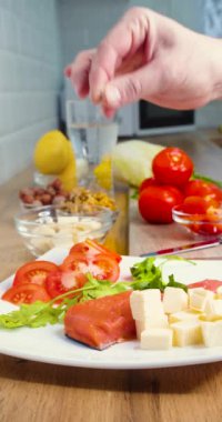 Close-up vertical video of a male hand sprinkles fish and cheese with salt. Keto diet and healthy eating concept for weight loss and fat control. Vertical 4k slow motion footage.
