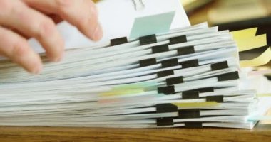 Office stillife - fingers fingering a large stack of paper documents. A person sorts through a stack of documents in search of the necessary folder for work. Hands close-up.