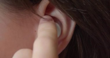Kulaklığı yakın çekimde takıyor. Genç bir kızın kulağı. Müzik dinlemek için küçük bir kulaklık takıyor. Modern gençlik ve onların kültürü. Clsoe-up ağır çekim 4k görüntü.