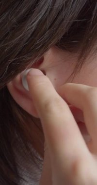Genç bir kızın kulağının dikey videosu. Müzik dinlemek için kulaklık takıyor. Modern gençlik ve onların kültürü. Yakın çekim yavaş çekim 4k görüntü.