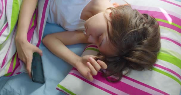 침대에 소녀는 깨어나자마자 스마트폰으로 미디어 메시지를 합니다 비디오는 온라인 네트워크에 — 비디오