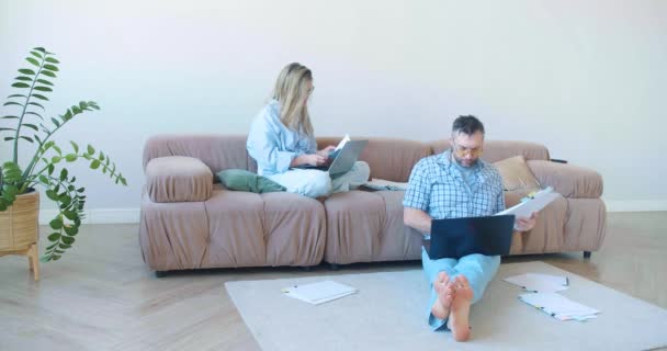 在家里工作的男人和女人 他们坐在家里的沙发上 带着手提电脑和文件 检查文档 并用计算机中的数据检查它们 60Fps 4K镜头 — 图库视频影像