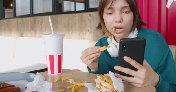 Egy Tinédzser Lány Sült Krumplit Eszik Beleesik Egy Okostelefon Képernyőjébe — Stock videók