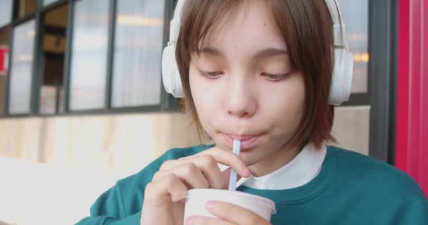 패스트푸드 카페에 소녀가 헤드폰을 음료수를 마시는 모습을 가까이 것이다 동영상 — 비디오