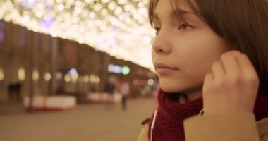 Kulaklık takan, akıllı telefon uygulamasından müzik seçen ve Noel 'in büyülü havasından keyif alan genç bir kızın yakın çekim videosu..