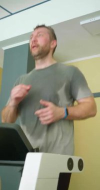 Spor salonunda koşu bandı egzersizi yapan orta yaşlı bir adamın dikey görüntüleri. Yavaş çekim dikey 4k görüntü.