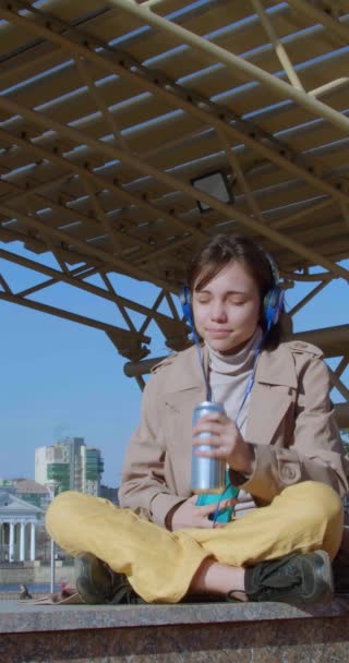 現実からデジタル世界への脱出とジャンクフード 10代の女の子が街を背景に屋上に座り ソーシャルメディアでチャットしながらエネルギードリンクを飲みます — ストック動画