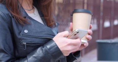 Tanımlanamayan genç bir kadın şehir caddesinde bankta oturuyor. İnternetten kahve içip mesajlar yolluyor. Yakın plan beyaz kadın, dışarıda akıllı telefon uygulamasında sosyal medyayı tarıyor. 4k görüntü