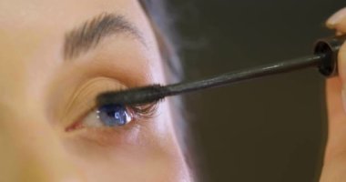 Güzel mavi gözlü kadın aynanın önünde kirpiklerini boyuyor. Yakın çekim görüntüsü. 4k görüntü.