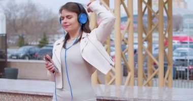 Genç iş kadını kulaklıkla müzik dinlerken dans ediyor. Çevrimiçi akıllı telefon uygulaması kullanarak. Yavaş çekim 4k video.