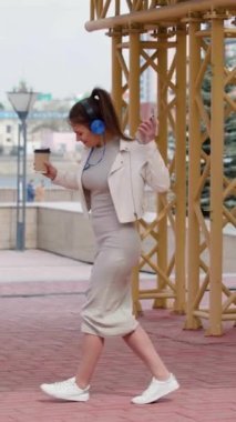 Kahve molası sırasında dans etmek. Çevrimiçi akıllı telefon uygulaması kullanarak kulaklıkla müzik dinlerken dans eden mutlu genç bir kadın. Yavaş çekim dikey 4k video.