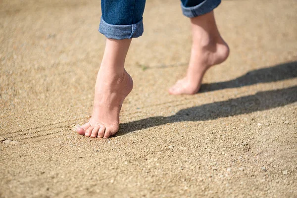 Woman walking barefoot on rough warm sand and little sharp stones. Close-up view.