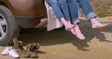 Bir çiftin ayakları, büyük şehrin gürültüsünden uzakta. Seyahat ve aşk doğada. Bir arabanın bagajında oturan çift. Bacaklarını kapat..