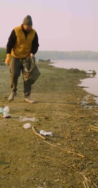 Çevreye önem vermek. Göl kıyısındaki çöpleri plastik bir torbayla temizliyorum. Nehirlerimizi ve göllerimizi temiz ve sağlıklı tutmanın önemi. Yavaş çekim dikey 4k görüntü.