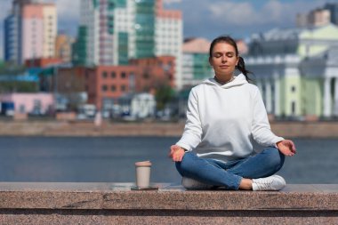 Genç bir kadın meditasyon yapıyor. Şehir gürültüsünden ve günlük koşuşturmadan dinleniyor. Büyük şehrin gürültüsünden, şehir yaşam tarzından kaçmak.