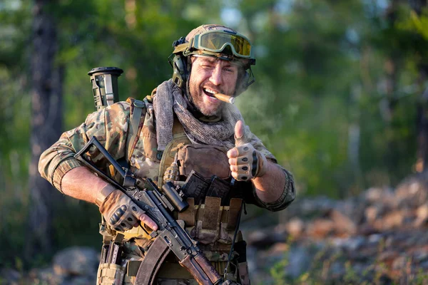微笑着现代雇佣兵士兵吸烟 微笑着 露出大拇指 一个留着胡子的中年男子穿着军用弹药 抽了一支雪茄 看着摄像机 垂直慢动作4K镜头 — 图库照片