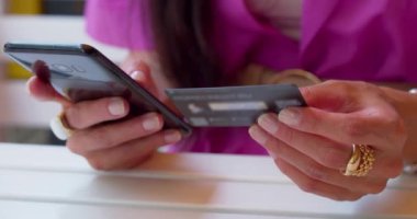 Akıllı telefon ve kredi kartı olan bir kadının yavaş çekim 4K görüntüsü. Çevrimiçi bir kafede alışveriş..
