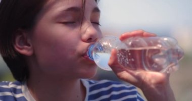 Sıcak bir yaz gününde plastik şişeden su içen genç bir kızın yakın çekimi. Yavaş çekim 4k görüntü.