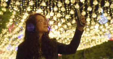 Noel arifesinde çevrimiçi video görüşmesi. Avrupa 'nın Noel süsleme ışıkları altında arkadaşlarıyla veya akrabalarıyla çevrimiçi video görüşmeleri sırasında genç bir kadın. Yavaş çekim 4k görüntü.