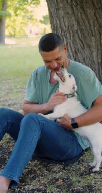 Akıl sağlığının bir yolu olarak evcil hayvanlarla sevgi ve iletişim. Parkta köpeğiyle birlikte orta yaşlı bir adam. Jack Russell Terrier sahibiyle oynuyor. Yavaş çekim dikey video.