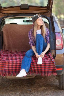 Akıl sağlığı ve yalnızlık. Dijital detoks konsepti. Kendinle baş başa kal. Genç bir kadın doğada arabasının bagajına çay doldurup dinleniyor. Dikey fotoğraf.