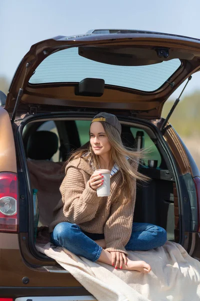 Run away from the noise of the city. Mental health and solitude in nature. Rest alone with yourself - a young woman drinks coffee rest in the trunk of her car in nature.