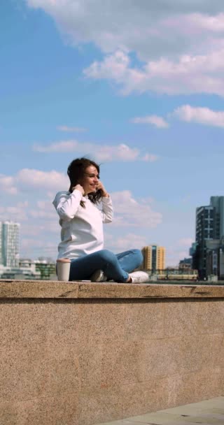 Eine Junge Frau Sitzt Mit Erhobenen Armen Vor Einem Stadtbild — Stockvideo