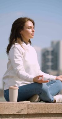 Gürültülü şehir manzarasının ortasında, genç bir kadın sessizlikte meditasyon yapıyor, saçları rüzgarda sallanırken nefesinin ritmiyle bir oluyor. Dijital dünyadan bağlantıyı kes.