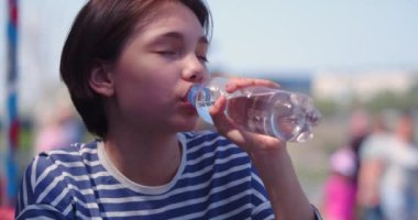 Plastik şişeden temiz su içen genç bir kız. Yavaş çekim 4k görüntü.