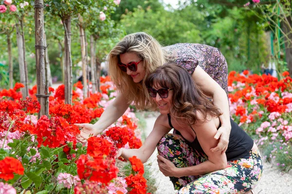 Kaksi Kaunista Keski Ikäinen Tyttöystäviä Vierailevat Puutarhassa Täynnä Kukkia Ranskassa — kuvapankkivalokuva