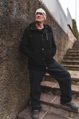 Olgun bir rap şarkıcısı büyük bir şehrin varoşlarında sokakta poz veriyor.