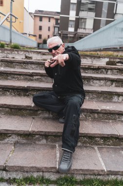 Yetişkin bir rap şarkıcısı büyük bir şehrin varoşlarında, merdivenlerde poz veriyor.