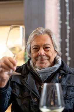 elegant mature man toasting with white wine sitting in outdoor cafe in winter