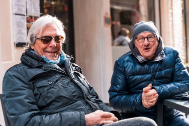 couple of happy retired attractive mature men relaxing sitting at outdoor cafe table in winter
