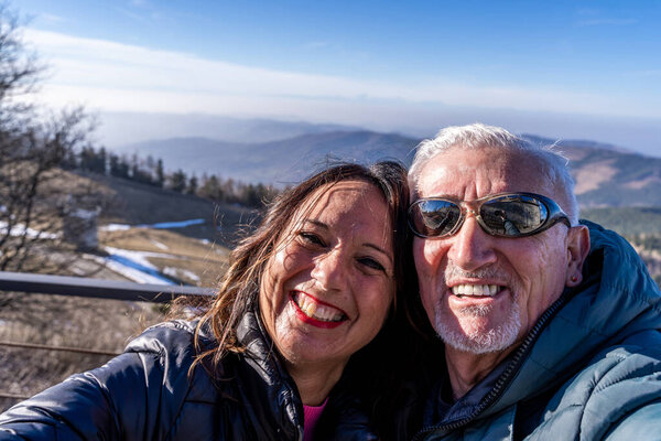 middle aged couple wearing winter clothes taking a selfie over a mountain - concept of happy people in vacation
