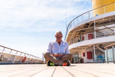 Bir yolcu gemisinin güvertesinde akıllı telefon kullanan mutlu, orta yaşlı bir adam. Seyahat ve tatil konsepti.