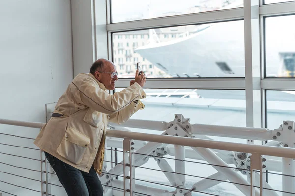 Φαλακρός Μεσήλικας Φωτογραφίζει Έξυπνο Τηλέφωνο Στην Αίθουσα Αναμονής Στο Λιμάνι — Φωτογραφία Αρχείου