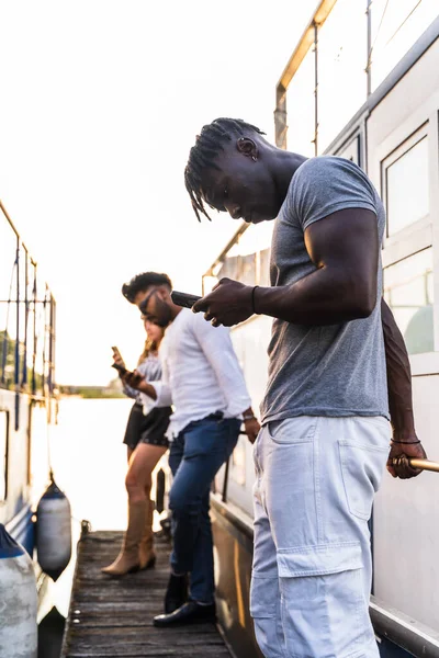 少数多种族朋友玩智能手机 在河上航行的小船上享受暑假的概念 — 图库照片
